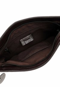 Interno di una borsa in pelle marrone con una texture liscia, tasca con zip, fodera in tessuto e etichetta in pelle del marchio.