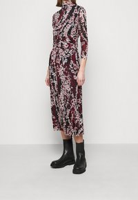 Kukkakuvioinen puolipitkä mekko korkealla kauluksella, jossa on musta pohja, vaaleanpunaisia ja burgundinvärisiä kukkia sekä muotoileva vyötärö. Yhdistetty mustiin nilkkureihin.