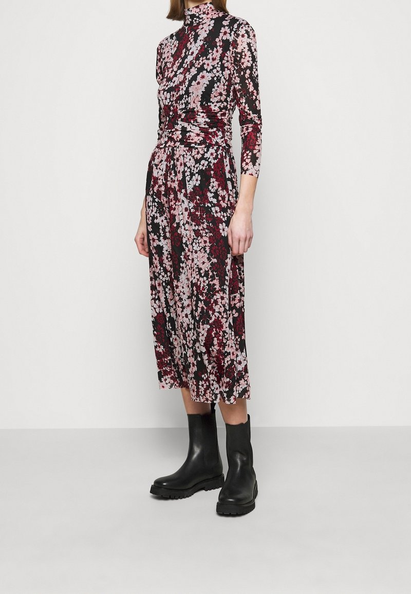 Kukkakuvioinen puolipitkä mekko korkealla kauluksella, jossa on musta pohja, vaaleanpunaisia ja burgundinvärisiä kukkia sekä muotoileva vyötärö. Yhdistetty mustiin nilkkureihin.