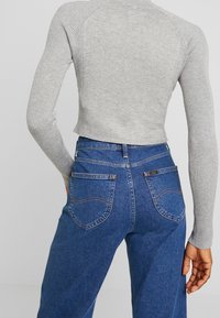 Suéter corto de canalé gris con mangas largas, combinado con jeans de mezclilla oscuros de cintura alta que cuentan con bolsillos y costuras en contraste.