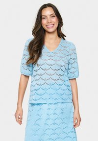 Top in pizzo azzurro chiaro con scollatura a V, maniche corte a sbuffo e motivo scallop. Il tessuto è trasparente con finitura texturizzata.