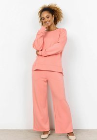 Top rosa chiaro a maniche lunghe con scollatura ampia e pantaloni abbinati a vestibilità ampia. Il materiale ha una texture morbida, con vestibilità rilassata e spacchi laterali.