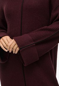 Maglione a maglia color bordeaux con bordi neri, caratterizzato da una trama a costine, maniche oversize e un design aperto davanti.