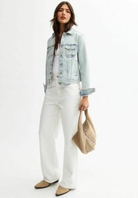 Lichtblauwe denimjack met twee voorzakken, witte fitted top, witte wijde broek en een tan tas met studs.