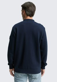 Felpa blu navy con motivo testurizzato, scollatura a girocollo e polsini a coste. Caratterizzata da un retro semplice e una vestibilità comoda, abbinata a jeans azzurri.