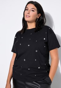 Camiseta negra de manga corta con adornos circulares plateados en un patrón disperso, fabricada en suave tejido de algodón y con un corte relajado.