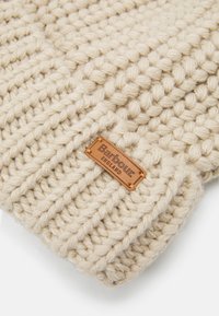 Pletená béžová čepice s texturovaným vzorem, která má na sobě hnědou koženou nálepku s vyraženými nápisy "Barbour" a "England".