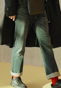 Jeans di denim in blu sbiadito con le maniche arrotolate, abbinati a scarpe da ginnastica nere e calzini rossi. Accessoriati con una borsa nera.