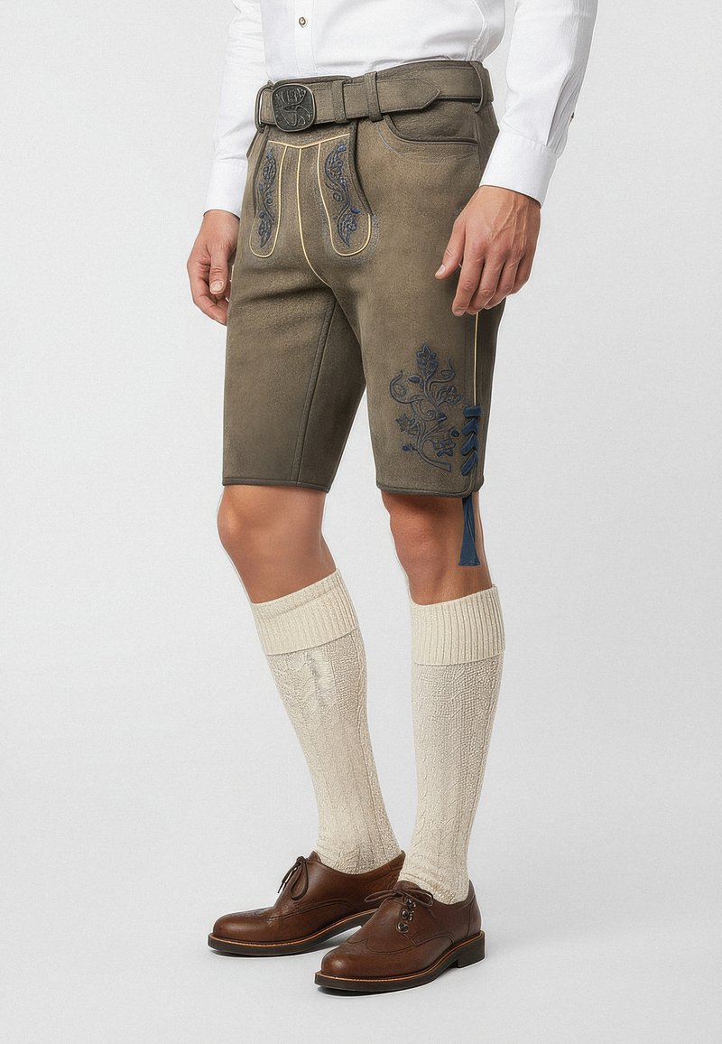 Bruna läderlederhosen med blomsterbroderi i blått, med ett bälte och knälång design, tillsammans med krämfärgade knästrumpor och bruna skor.