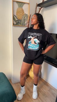 Camiseta negra de gran tamaño con un colorido estampado de "Luna de Medianoche", combinada con pantalones cortos negros y botas de plataforma blancas. Textura plana, diseño casual.