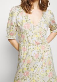 Blumenkleid mit V-Ausschnitt, Puffärmeln und einem sanften gelben Hintergrund mit Mustern aus rosa, blauen und grünen Blumen.