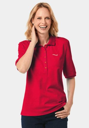 Rode poloshirt met korte mouwen, drieknoopsluiting en geborduurd logo. Zachte textuur, casual pasvorm, gecombineerd met donkere jeans.