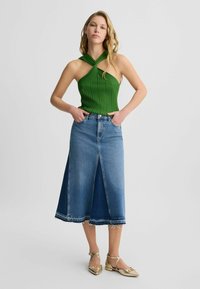 Zelený žebrovaný halter top s krouceným designem, spárovaný s mid-length denimovou sukní s předním rozparkem a třepeným lemem. Zlaté ploché boty.