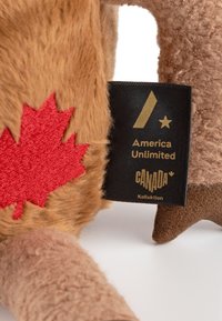 Brown plush toy with a red maple leaf patch, featuring a black label that reads "America Unlimited" and "CANADA." Textured fur surface.