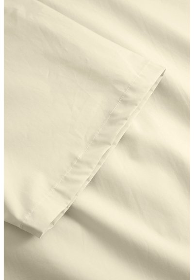 Tissu de couleur crème clair avec une texture lisse, présentant un ourlet piqué et des plis subtils, tombant en diagonale à travers le cadre.