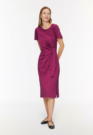 Mauve knielanges Kleid mit kurzen Ärmeln, das ein verdrehtes Detail an der Taille und einen seitlichen Schlitz aufweist. Das Material wirkt weich und glatt.