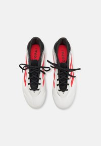 Scarpe da ginnastica bianche con lacci neri, accenti rossi e una texture liscia. Presentano il logo e strisce sui lati.