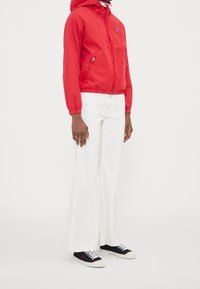 Czerwona, lekka kurtka z kapturem i zamkiem błyskawicznym, z elastycznymi mankietami, w połączeniu z białymi spodniami w kształcie dzwonów i czarnymi butami z białą podeszwą i sznurowadłami.