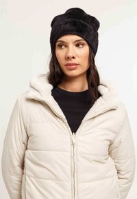 Giacca a vento in beige chiaro, con chiusura a zip e cappuccio foderato in pelliccia; berretto nero felpato con tessuto testurizzato e orecchie a forma di orso.
