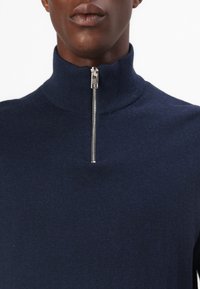 Marineblauer Strickpullover mit hohem Kragen und silbernem Reißverschluss, der eine glatte Textur und eine figurbetonte Passform bietet.