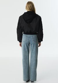 Zwarte cropped hoodie met ribbelzoom; lichtblauwe highwaisted jeans met een rechte pasvorm en twee achterzakken. Minimalistisch ontwerp.