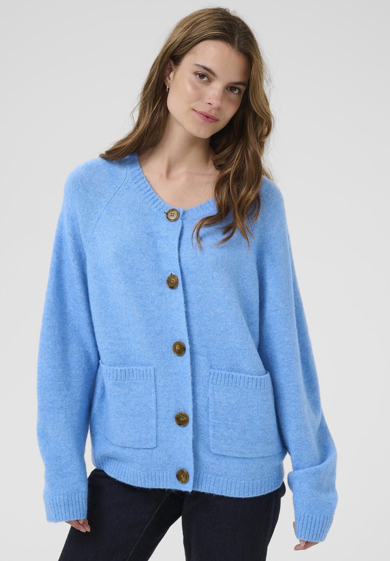 Lyseblå strikket cardigan med V-hals, fire store brune knapper, ribbede manchetter og to frontlommer. Blødt, struktureret stof.