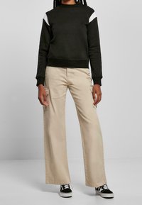 Sudadera negra con acentos blancos en los hombros, combinada con pantalones cargo de pierna ancha beige que presentan bolsillos laterales. Zapatillas negras completan el conjunto.