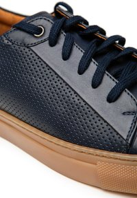Granatowe skórzane sneakersy z perforowaną teksturą, brązową gumową podeszwą, kontrastującymi beżowymi akcentami oraz płaskimi granatowymi sznurówkami. Okrągły kształt czubka.