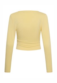 Haut court à manches longues jaune pâle avec encolure bateau, tissu lisse et détail froncé subtil à la taille au dos.