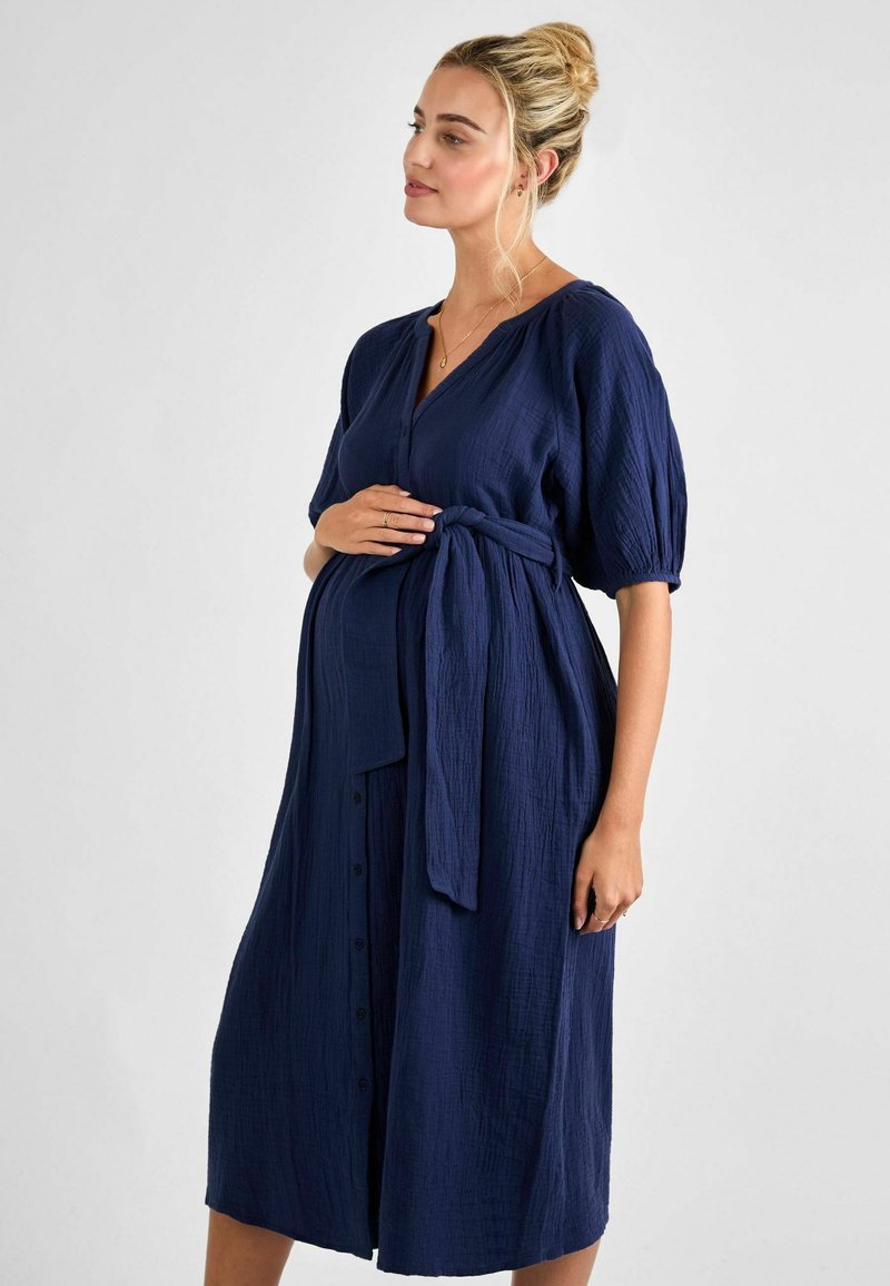 Abito premaman strutturato blu navy con maniche a palloncino corte, vita con nastro e bottoni frontali, realizzato in un materiale morbido e leggero.