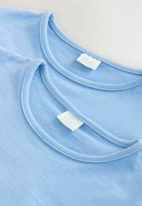 Deux T-shirts bleu clair empilés, avec un col rond et une texture en coton doux ; étiquettes visibles avec le nom de la marque "NEXT."