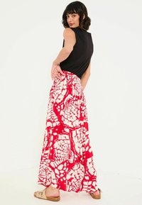 Maxi-Rock in einem auffälligen rot-weißen abstrakten Muster, mit einem fließenden Design und einem elastischen Bund, kombiniert mit einem schwarzen ärmellosen Top.