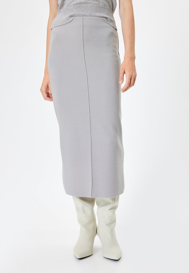Jupe midi grise à côtes avec une silhouette ajustée, présentant une taille sans couture et une coupe droite. Associée à des bottes blanches jusqu'aux genoux.