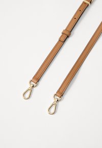 Tan leren band met gouden metalen sluitingen, met een gladde textuur, verstelbare lengte en een stikselafwerking langs de randen.