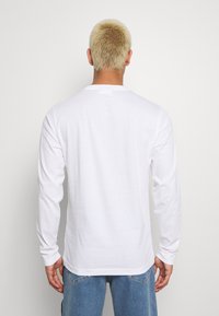 Long-sleeve white t-shirt made of cotton, featuring a round neckline and a relaxed fit. Smooth texture and simple design, no patterns or accents.