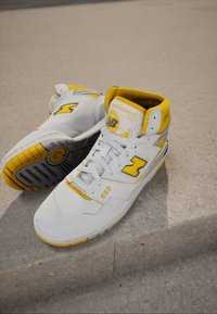 Sneaker alte bianche in pelle, con dettagli gialli, colletto imbottito e suola in gomma grigia testurizzata con il numero "650".