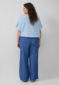 Hellblaues, kurzärmliges Oberteil kombiniert mit weitgeschnittenen blauen Leinenhosen. Weiche Textur, lockere Passform und minimale Details.