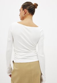 White long-sleeve top with a ribbed texture and an off-shoulder design. The fabric appears soft, complementing a beige skirt.