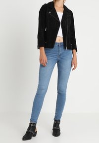 Zwarte suède motorjack met halflange mouwen, gecombineerd met lichtblauwe skinny jeans en zwarte sleehakken met studs.