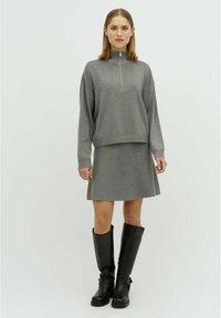 Grijze zip-neksweater gecombineerd met een bijpassende grijze rok, aangevuld met kniehoge leren zwarte laarzen. Gladde textuur en ontspannen fit.