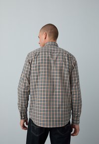 Chemise à manches longues à carreaux beige, marine et vert avec col boutonné et ourlet arrondi. Le tissu présente un motif à carreaux.