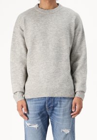 Grå stickad tröja med rund halsringning och ribbade ärmslut och nederkant, matchad med blå slitna denimjeans. Mjuk struktur uppenbar.