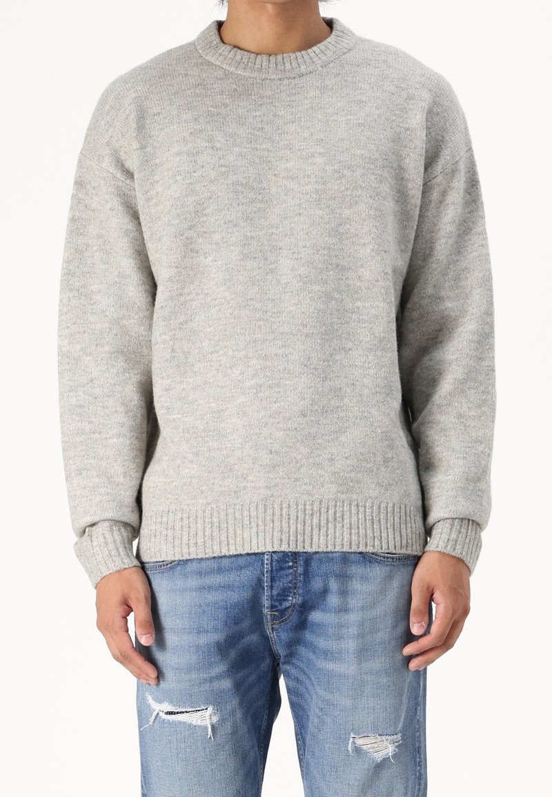 Grå stickad tröja med rund halsringning och ribbade ärmslut och nederkant, matchad med blå slitna denimjeans. Mjuk struktur uppenbar.