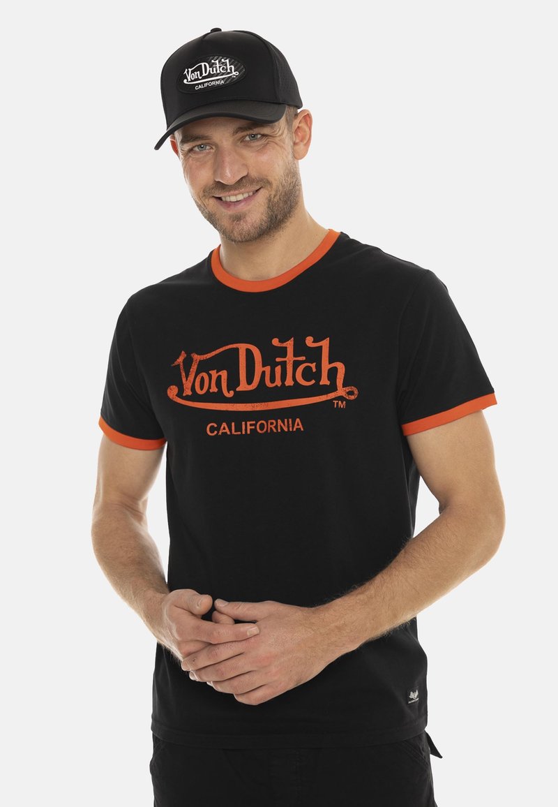T-shirt noire avec des bordures orange arborant le logo "Von Dutch CALIFORNIA". Associé à une casquette noire affichant le même logo en blanc.