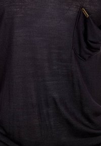 T-shirt nera realizzata in tessuto morbido, con una piccola tasca sul lato sinistro del petto decorata con un accento dorato e una vestibilità comoda.