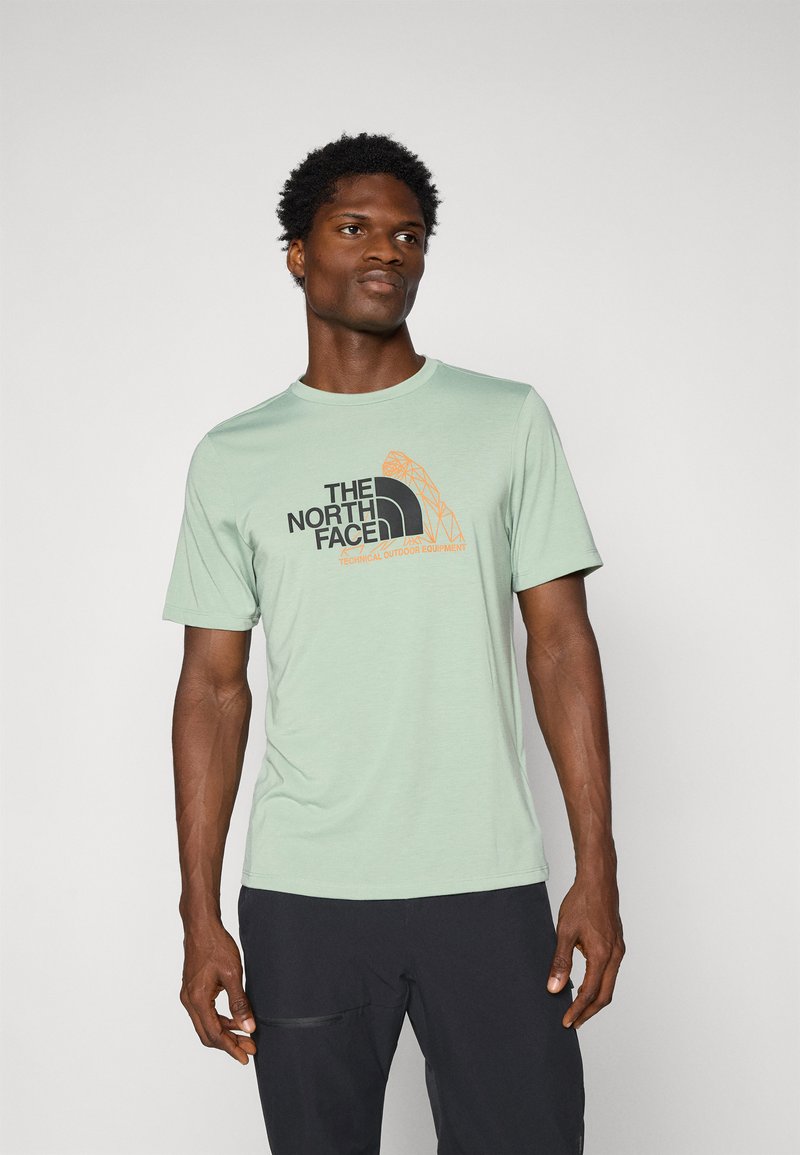 Camiseta de manga corta verde claro con un logotipo gráfico negro y naranja en la parte delantera. Material suave, cuello redondo y corte regular.