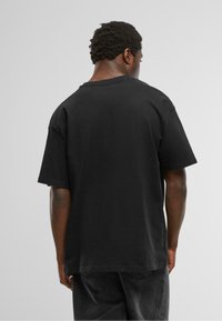 Zwarte katoenen t-shirt met een relaxte pasvorm, korte mouwen en een ronde halslijn, gezien van achteren tegen een neutrale achtergrond.