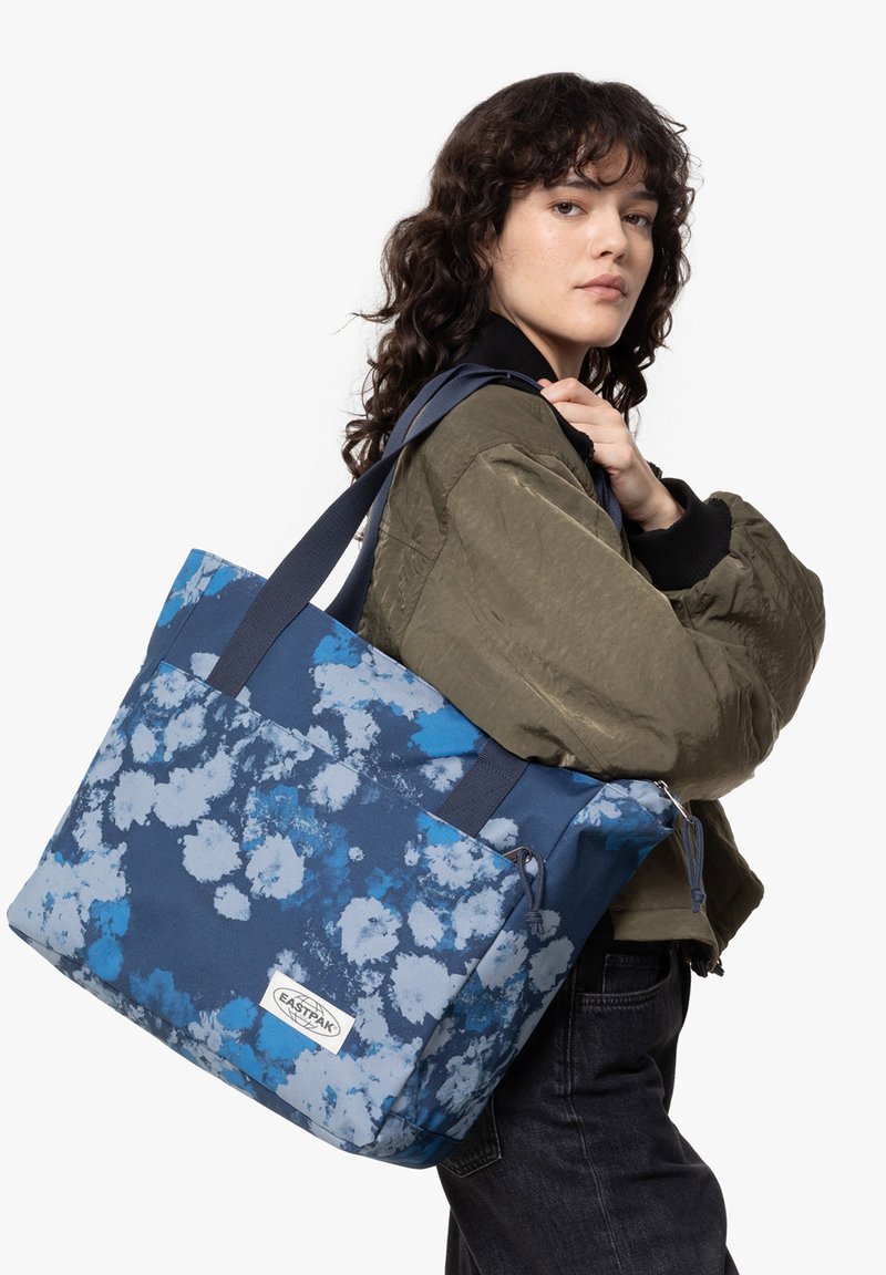 Sac fourre-tout à motif floral bleu de forme rectangulaire, fabriqué en tissu durable. Il dispose de deux poignées et d'une fermeture éclair.