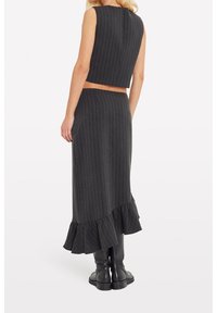 Černý pruhovaný dvoudílný outfit, který obsahuje zkrácený top bez rukávů a sukni do kolen s volánkovým lemem. Outfit je doplněn nad kolena sahajícími botami.