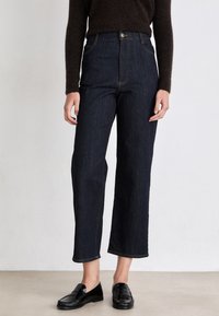 High-waisted dark blue jeans with a straight leg cut, contrasting stitching, and a button closure, paired with black loafers.